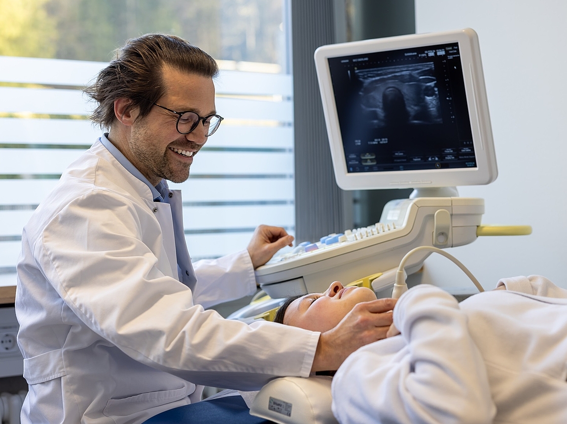 Untersuchung einer Patientin Ein Arzt untersucht die Schilddrüse mithilfe von Ultraschall einer Patientin.