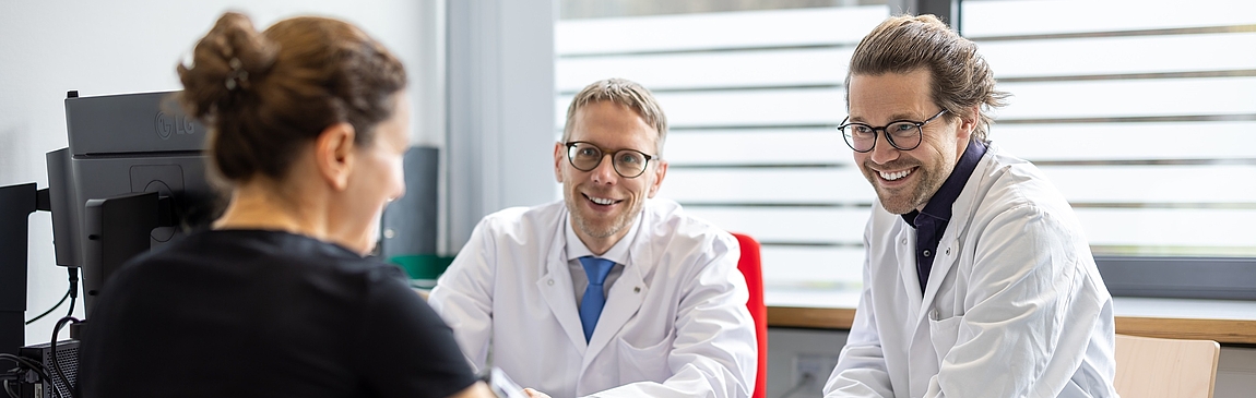 Eine Patientin sitzt zwei Ärzten gegenüber und wird mit dem Nachblutungsdetektor untersucht.